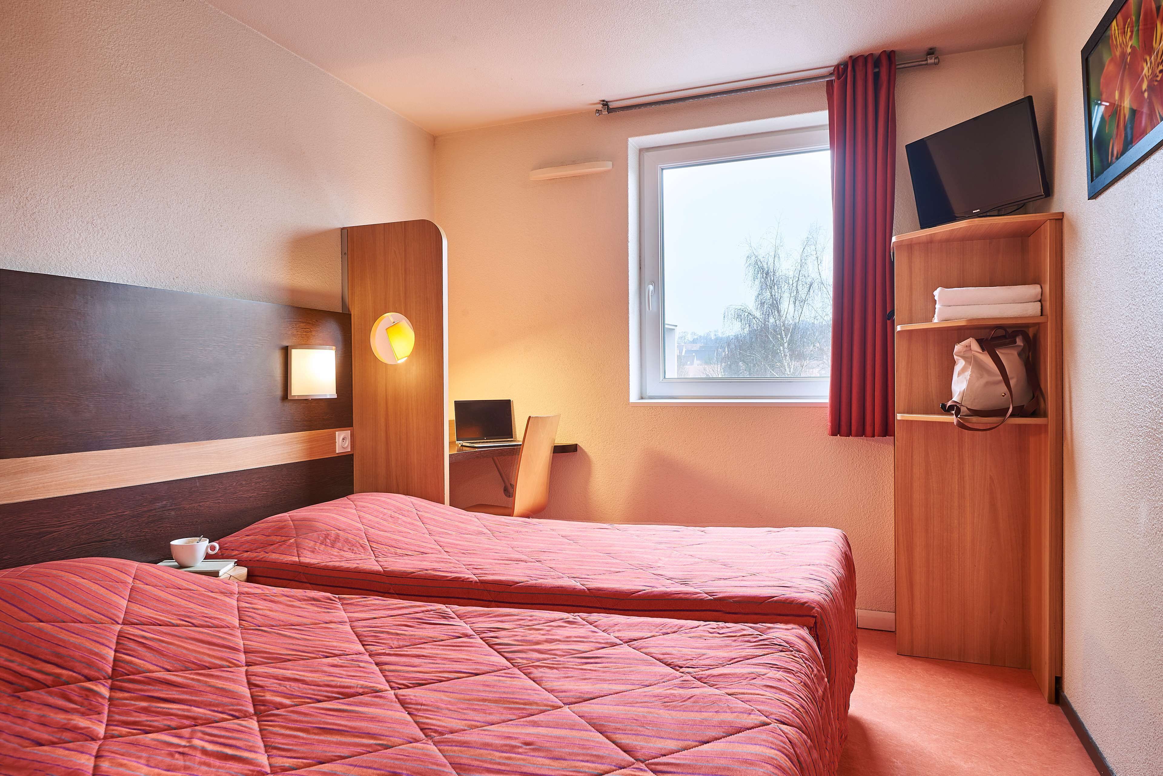 A hotel room with a large bed, a desk, a chair, a TV, and a wardrobe.