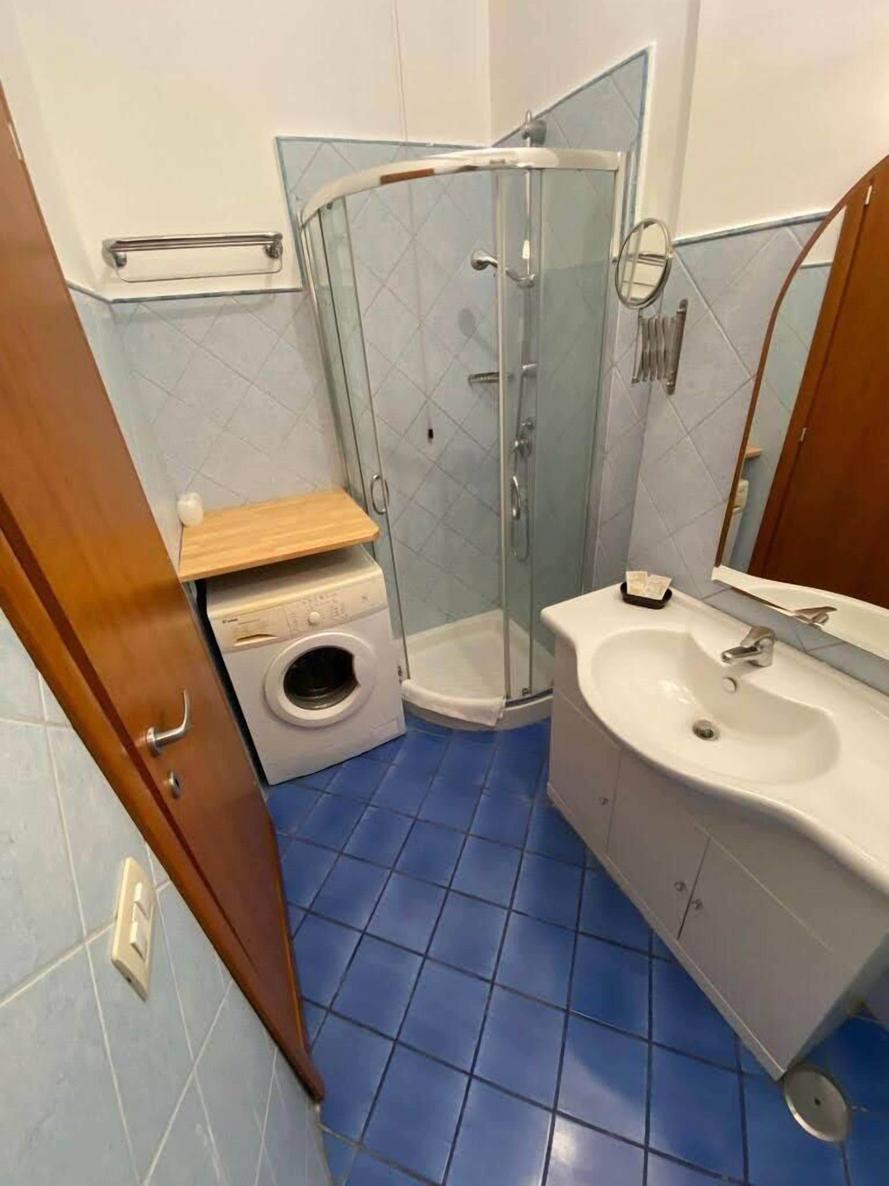 A bathroom with a glass shower enclosure, a washing machine, and a sink.