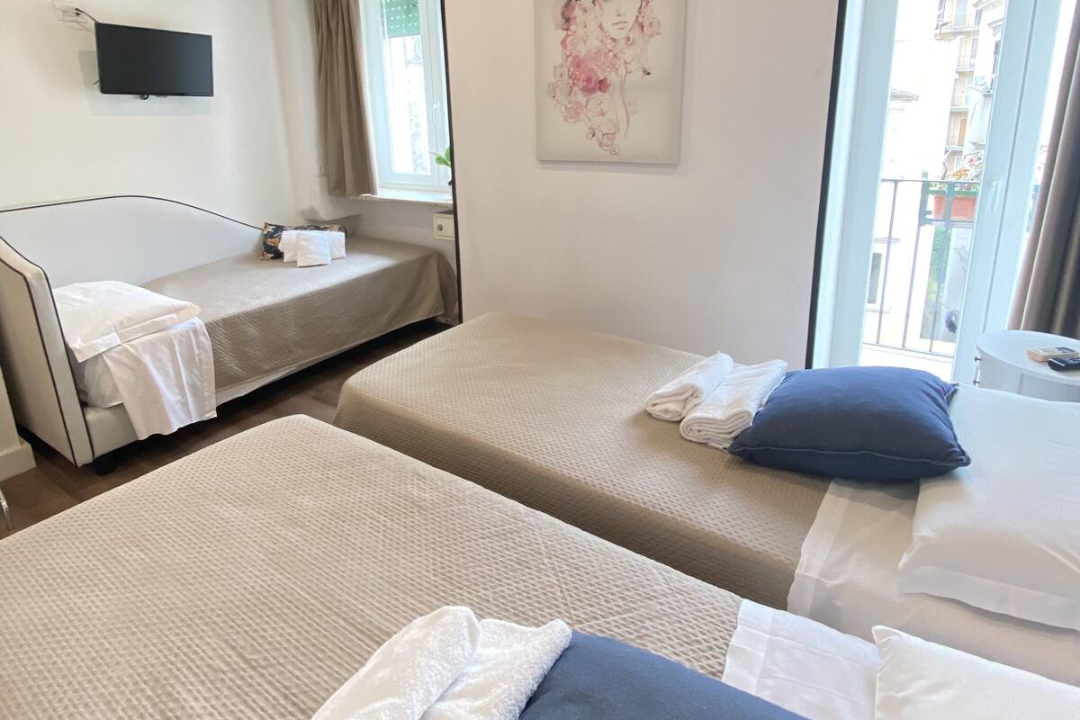 Une chambre d’hôtel avec deux lits, un téléviseur à écran plat, un appareil de climatisation, un tableau et une fenêtre donnant sur des immeubles.