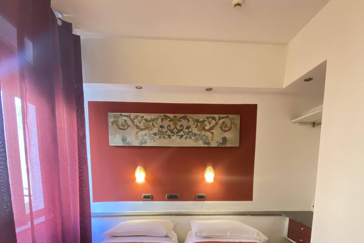 Une chambre d’hôtel avec deux lits simples, un élément décoratif mural et deux lampes fixées au mur.