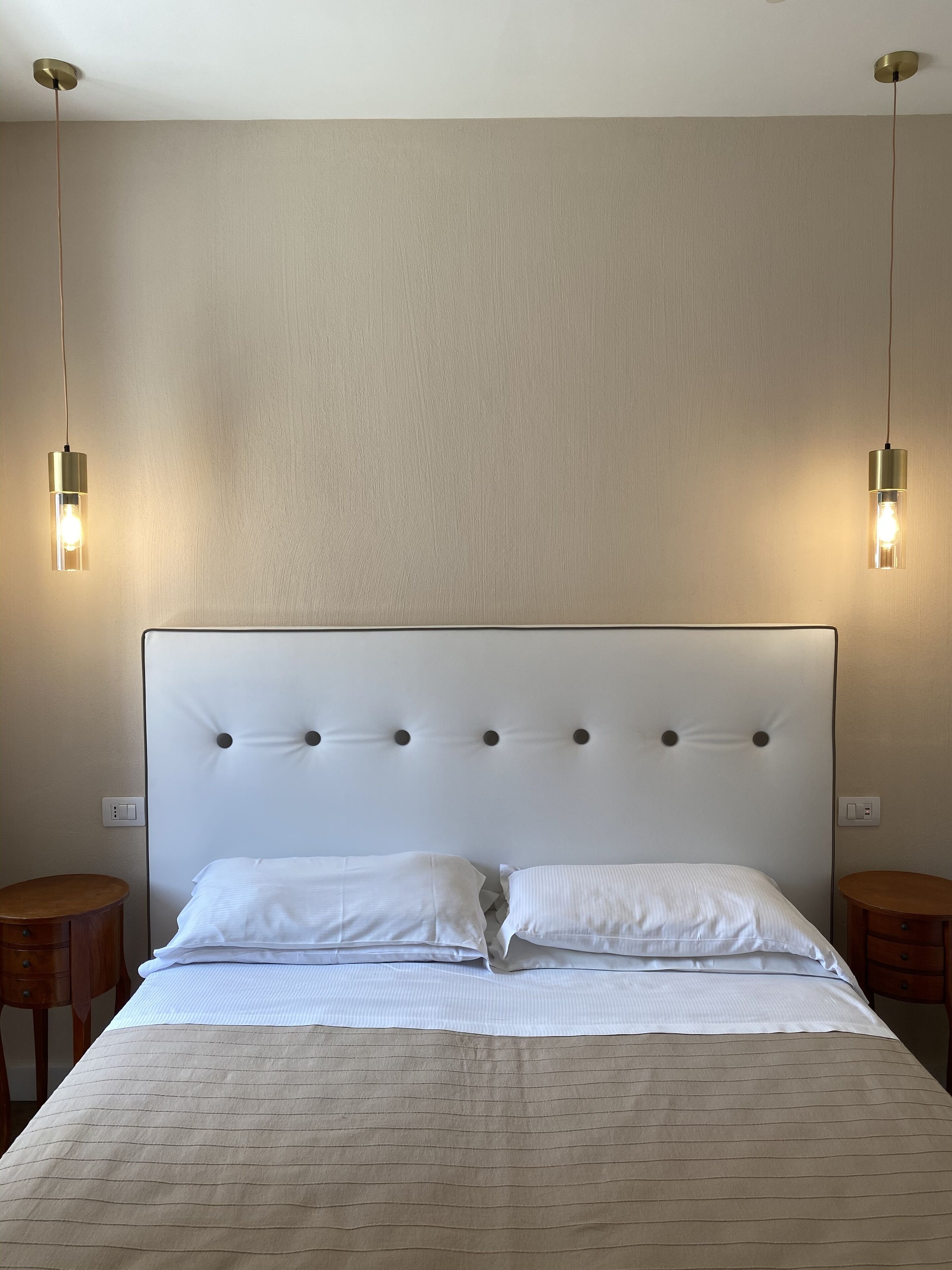 A neatly made bed with a tufted headboard, two bedside tables, and two wall-mounted lights.
