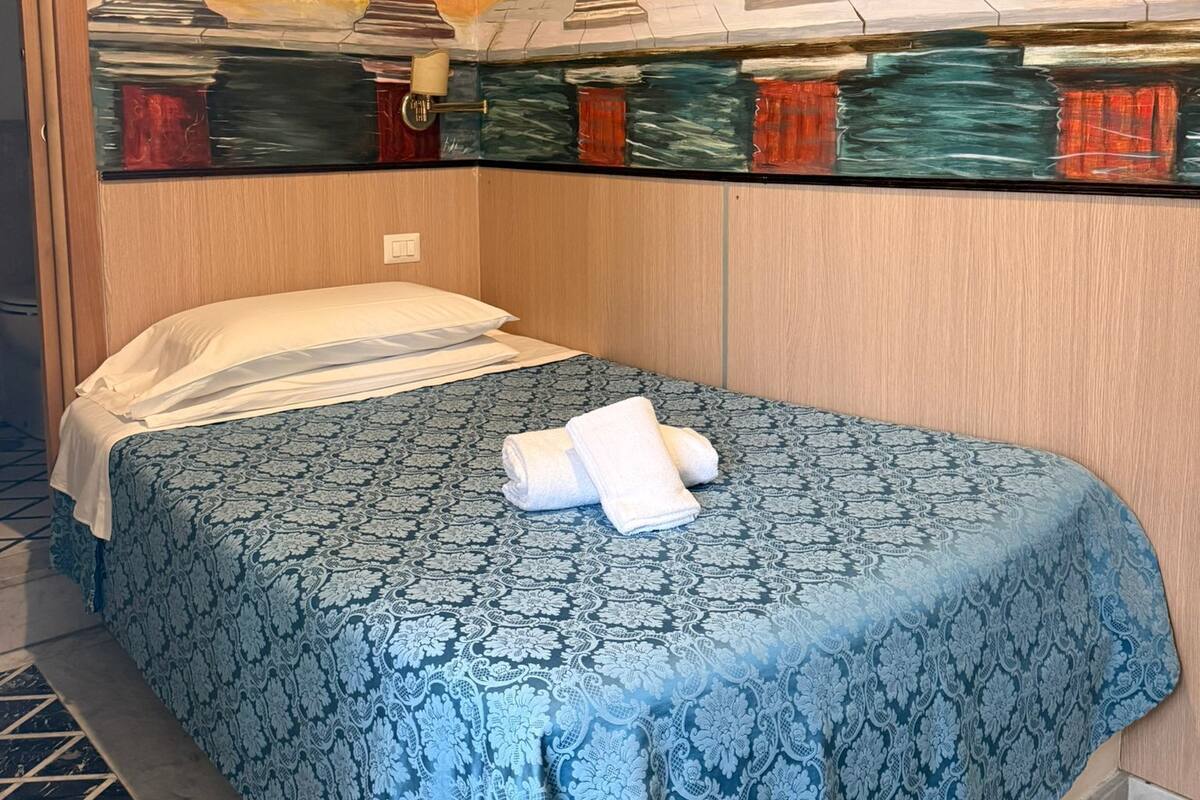 Une chambre d’hôtel avec un lit, une couvre-lit à motifs bleus et une fresque représentant un jardin sur le mur.