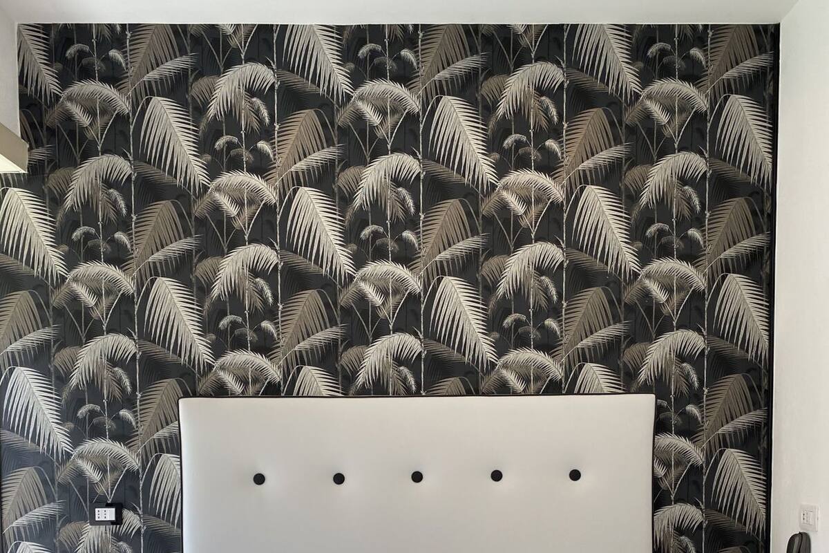 Un lit avec une tête de lit blanche, un oreiller foncé et un papier peint à motifs.
