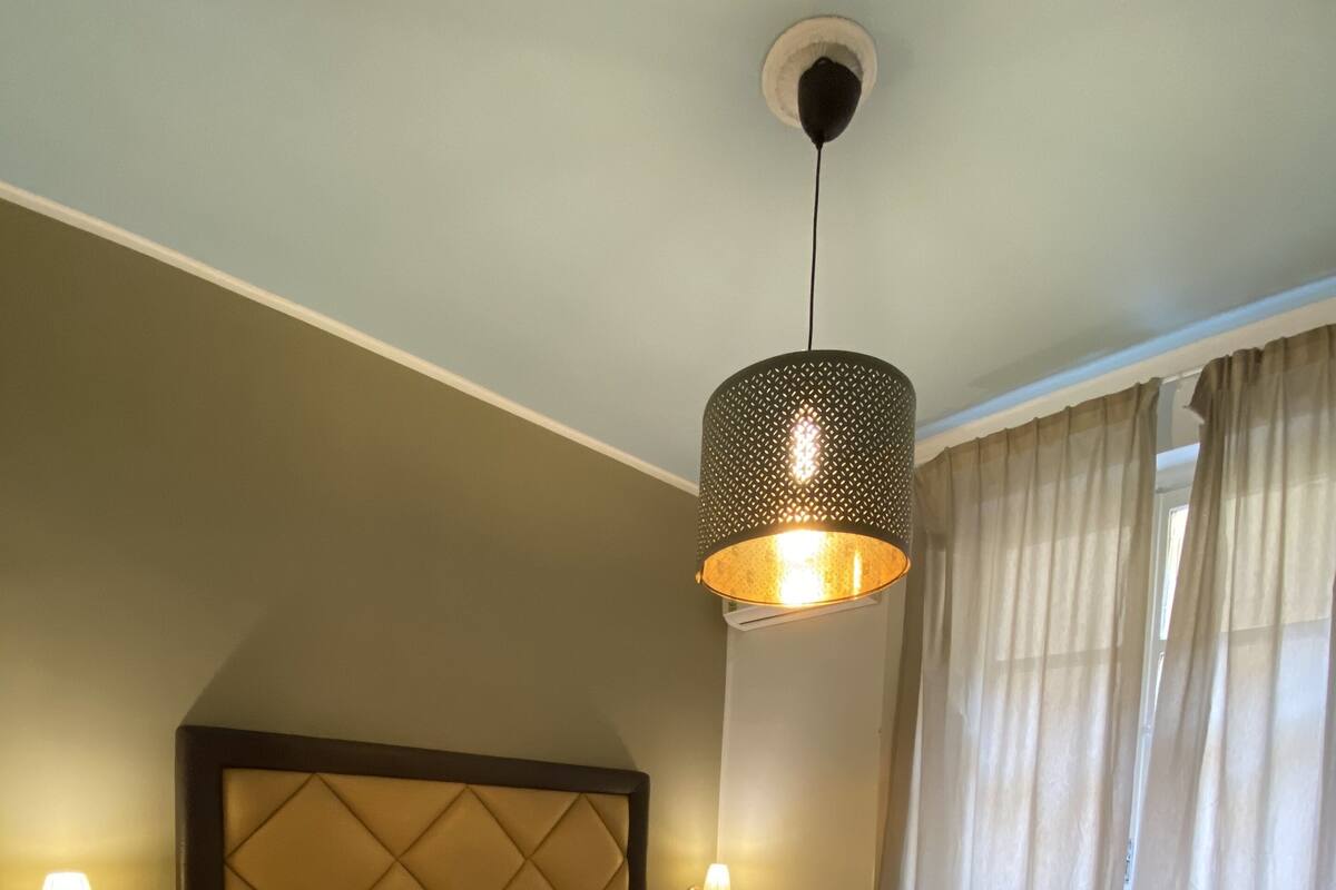 Une chambre d’hôtel avec un grand lit, une tête de lit, une table de chevet avec une lampe, un téléphone et une fenêtre avec des rideaux.
