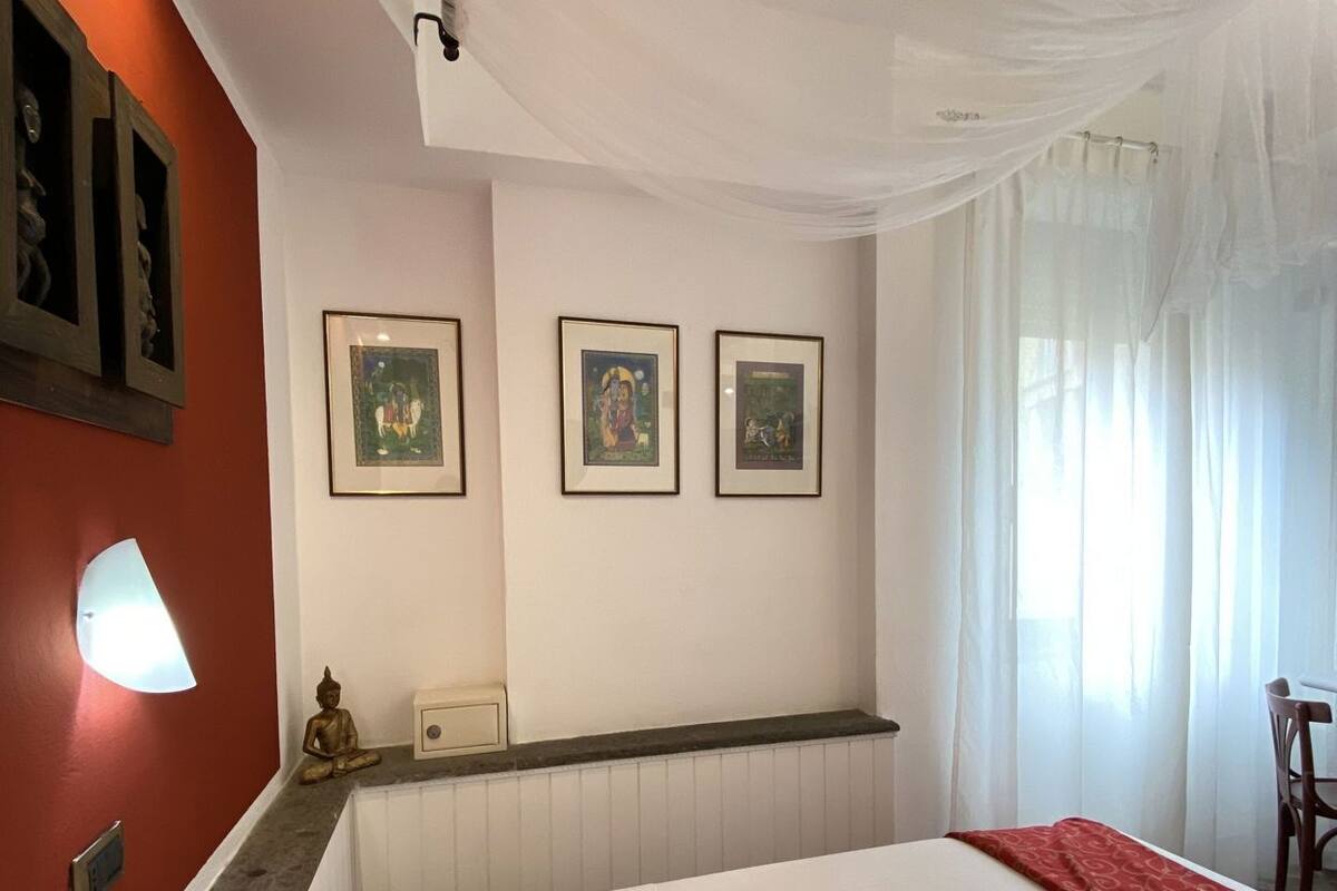 Une chambre d’hôtel avec un grand lit, une lampe fixée au mur, une statue de Bouddha et trois tableaux encadrés accrochés au mur.
