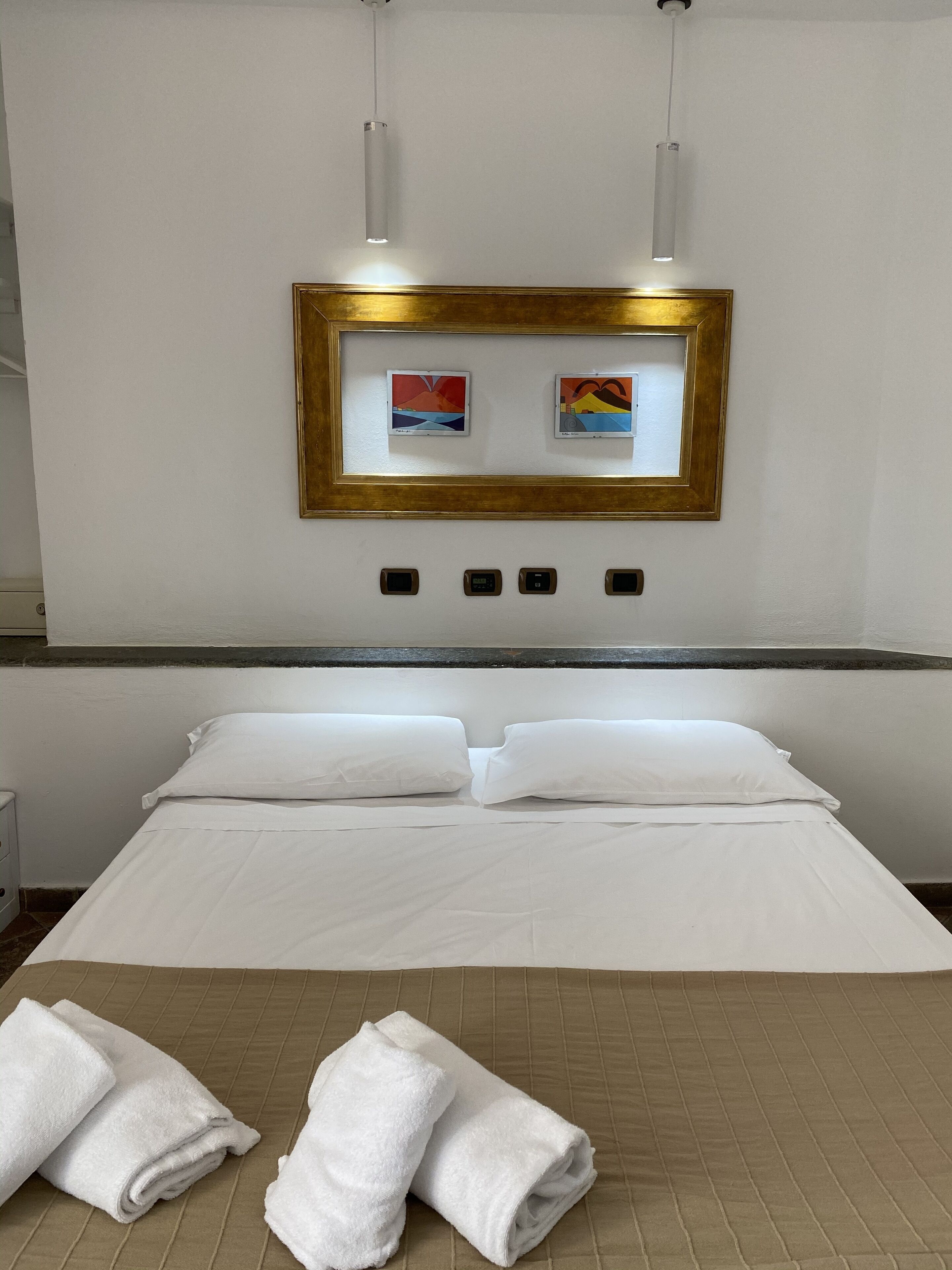 A hotel room with a bed, two paintings on the wall, a control panel, and two towels on the bed.