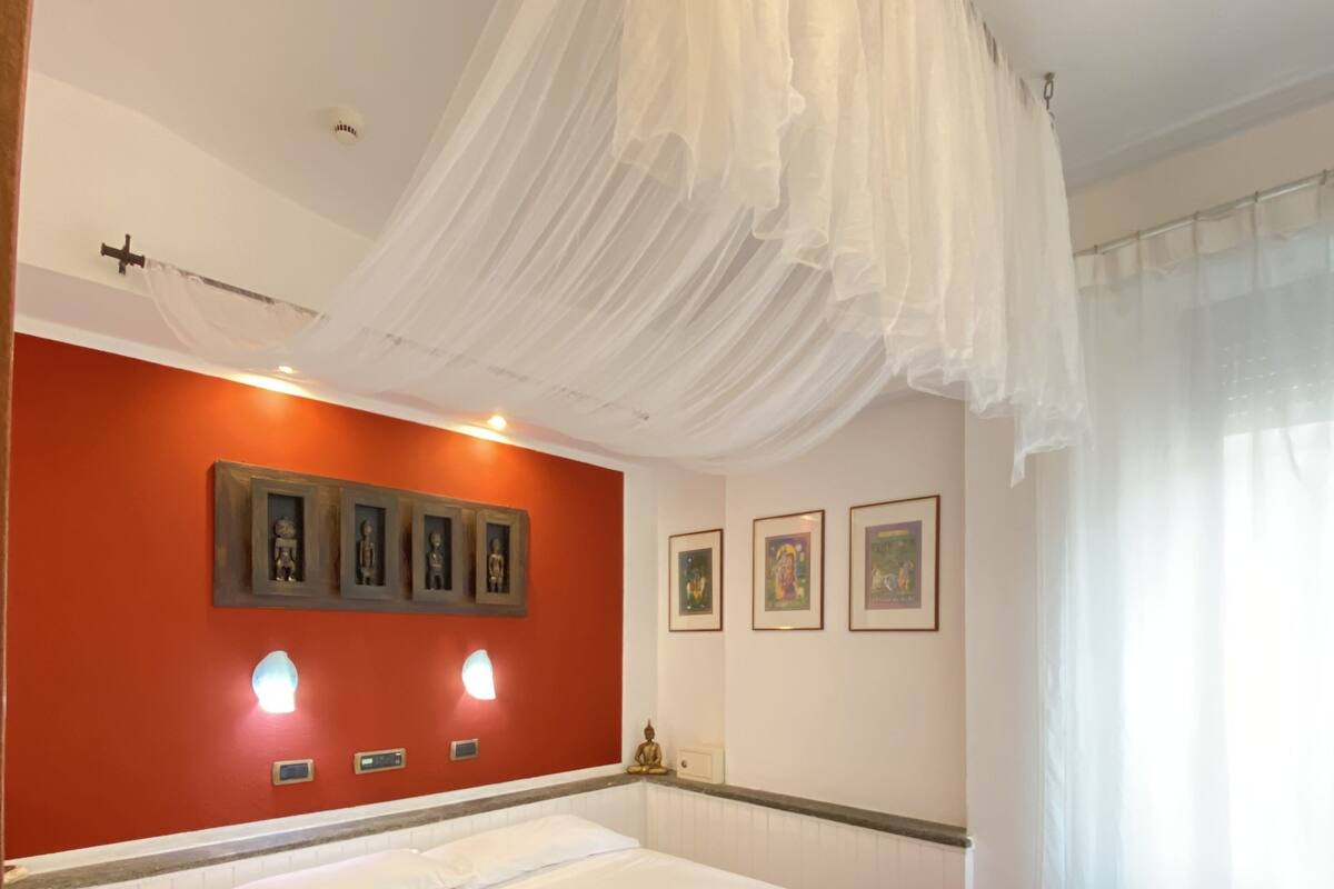 Une chambre d’hôtel avec un lit, un mur d’accent rouge, des tableaux encadrés et un baldaquin.