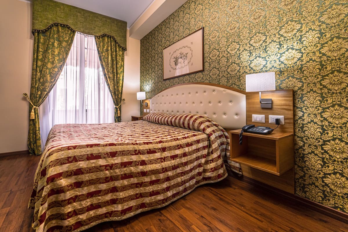 A bedroom with a large bed, a wooden nightstand, a telephone, and a wall-mounted lamp.