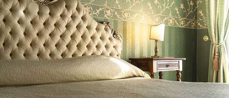 A bed with a tufted headboard, a bedside table with a lamp, and green patterned wallpaper.