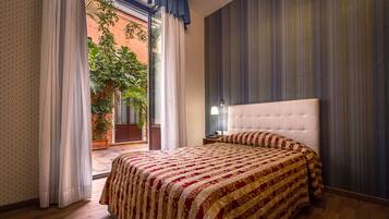 Un dormitorio con una cama grande, una mesita de noche, una ventana con cortinas y vistas a un jardín.