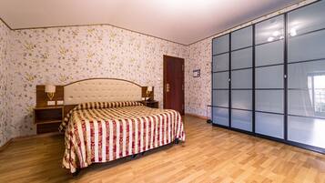Camera da letto con un letto, pavimento in legno, carta da parati a motivi floreali, un armadio e una porta.