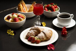 A breakfast setting with croissants, strawberries, a glass of red juice, and a cup of coffee on a dark table.