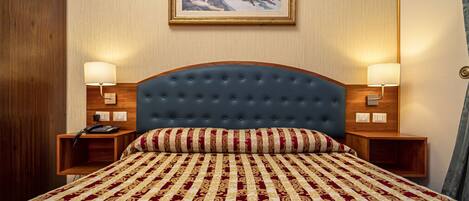 A hotel room with a large bed, two bedside tables with lamps, a wooden wardrobe, and a framed picture on the wall.