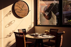 Un comedor con una mesa redonda, dos sillas, un reloj de pared de madera y una ventana con detalles decorativos.
