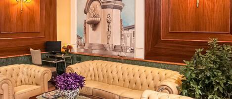 A lobby with a beige sofa, a coffee table with a vase, and a large mural of a statue.