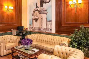 Un'area di benvenuto con un divano color beige, un tavolino da caffè con un vaso, e un grande murale raffigurante una statua.