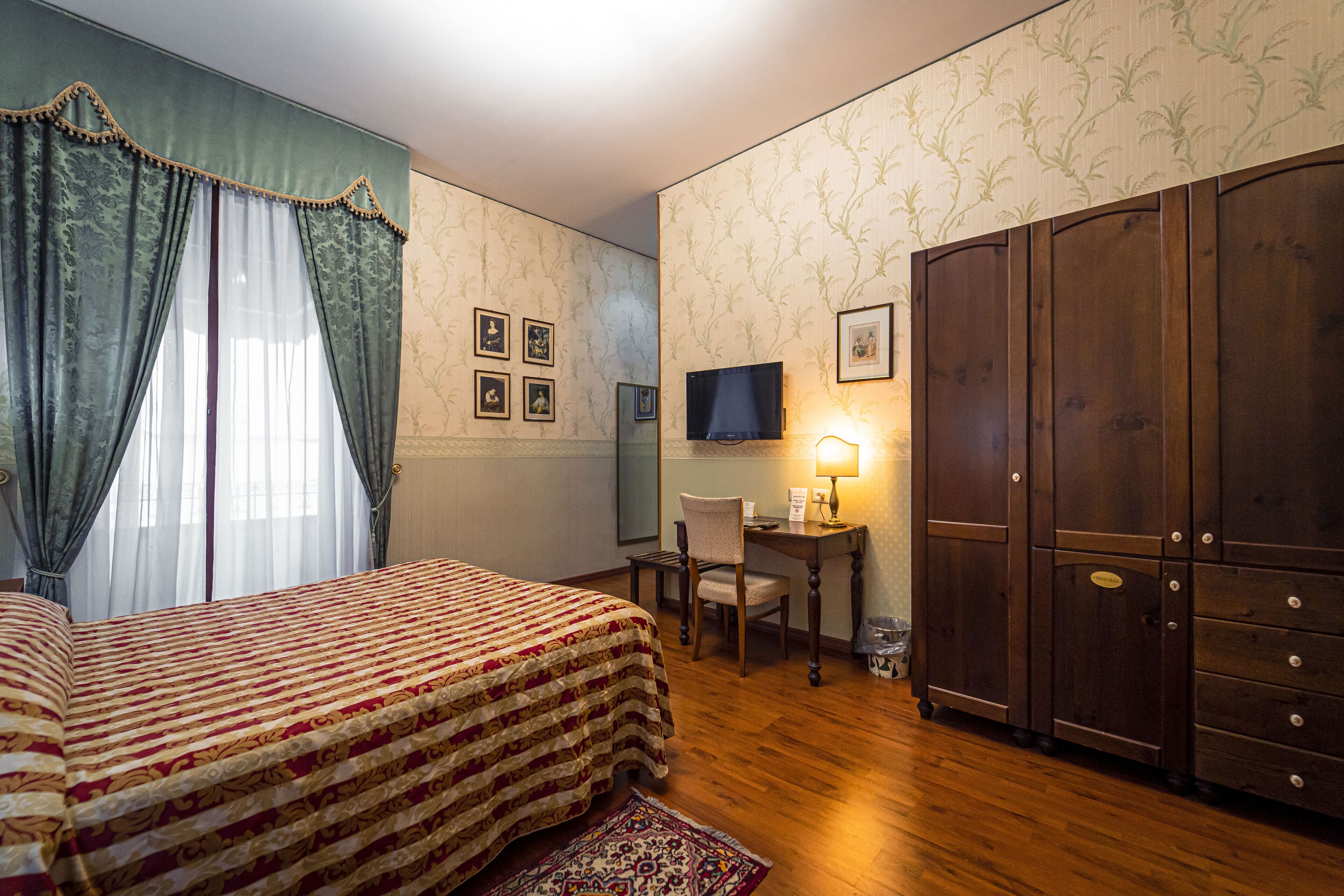 A hotel room with a bed, a desk with a chair, a television, and a wardrobe.