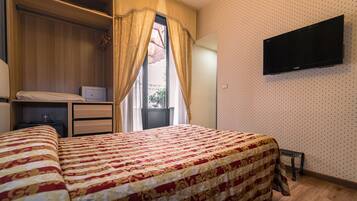 Una camera da letto con un letto, un armadio, un comodino, una TV a parete e una finestra con tende.