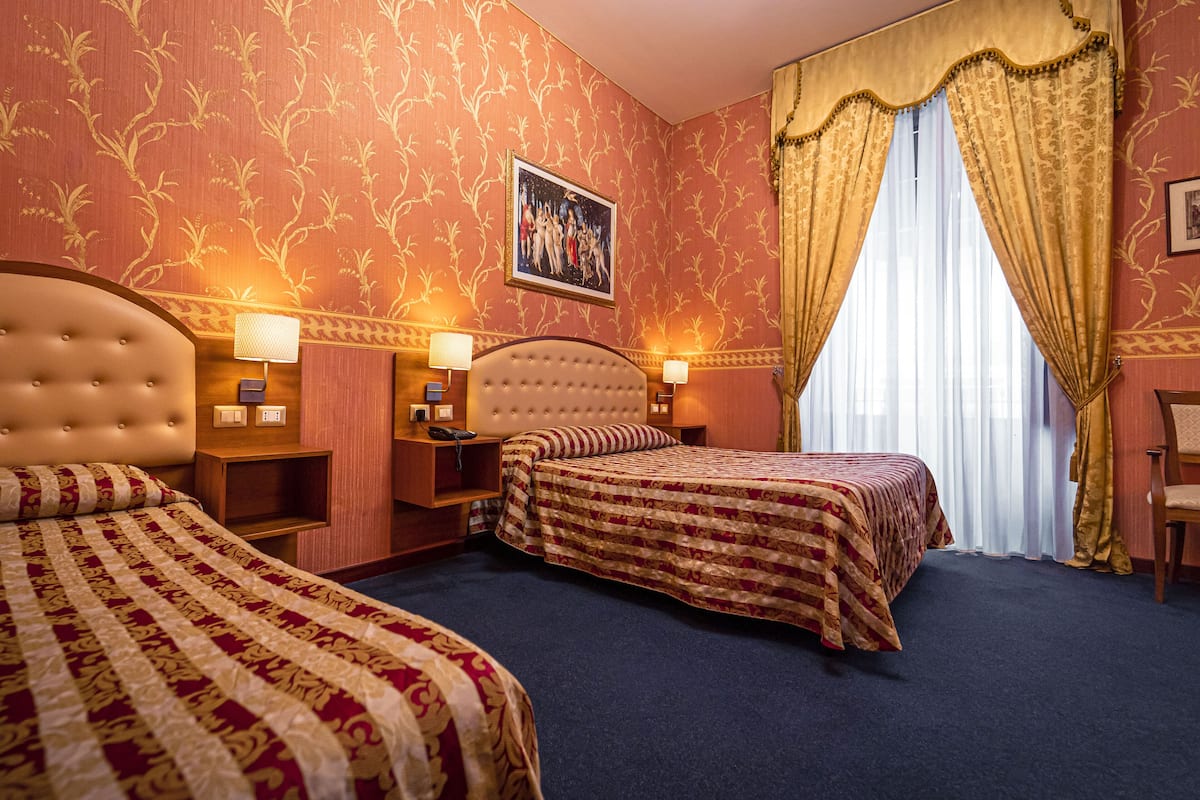 A hotel room with two beds, a large window with curtains, a painting on the wall, and bedside lamps.