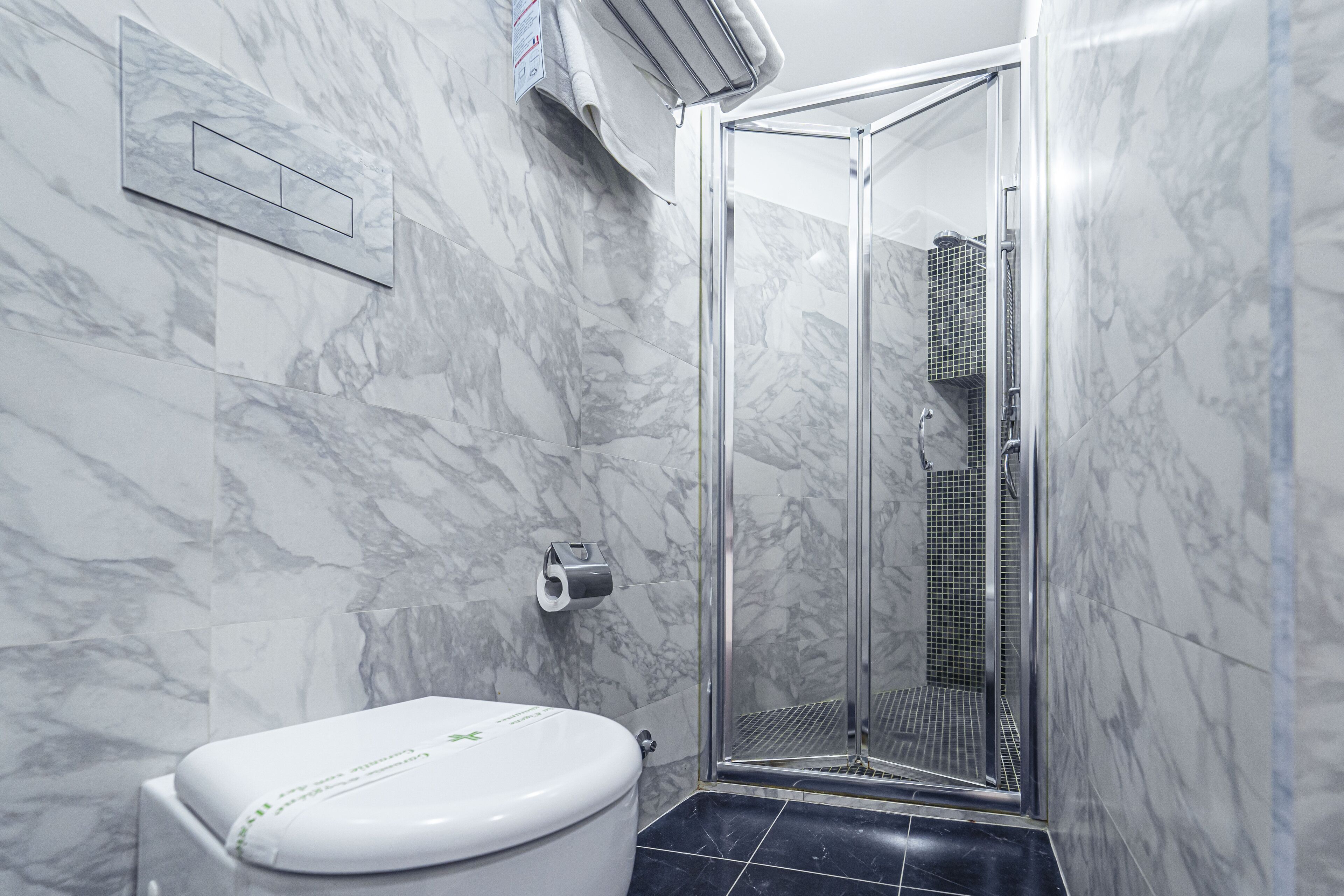 Un baño con inodoro, ducha con puerta de cristal y paredes de mármol.