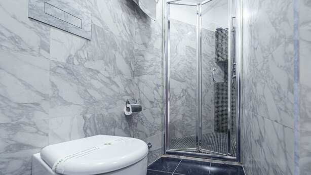 A bathroom with a toilet, a shower with a glass door, and marble walls.