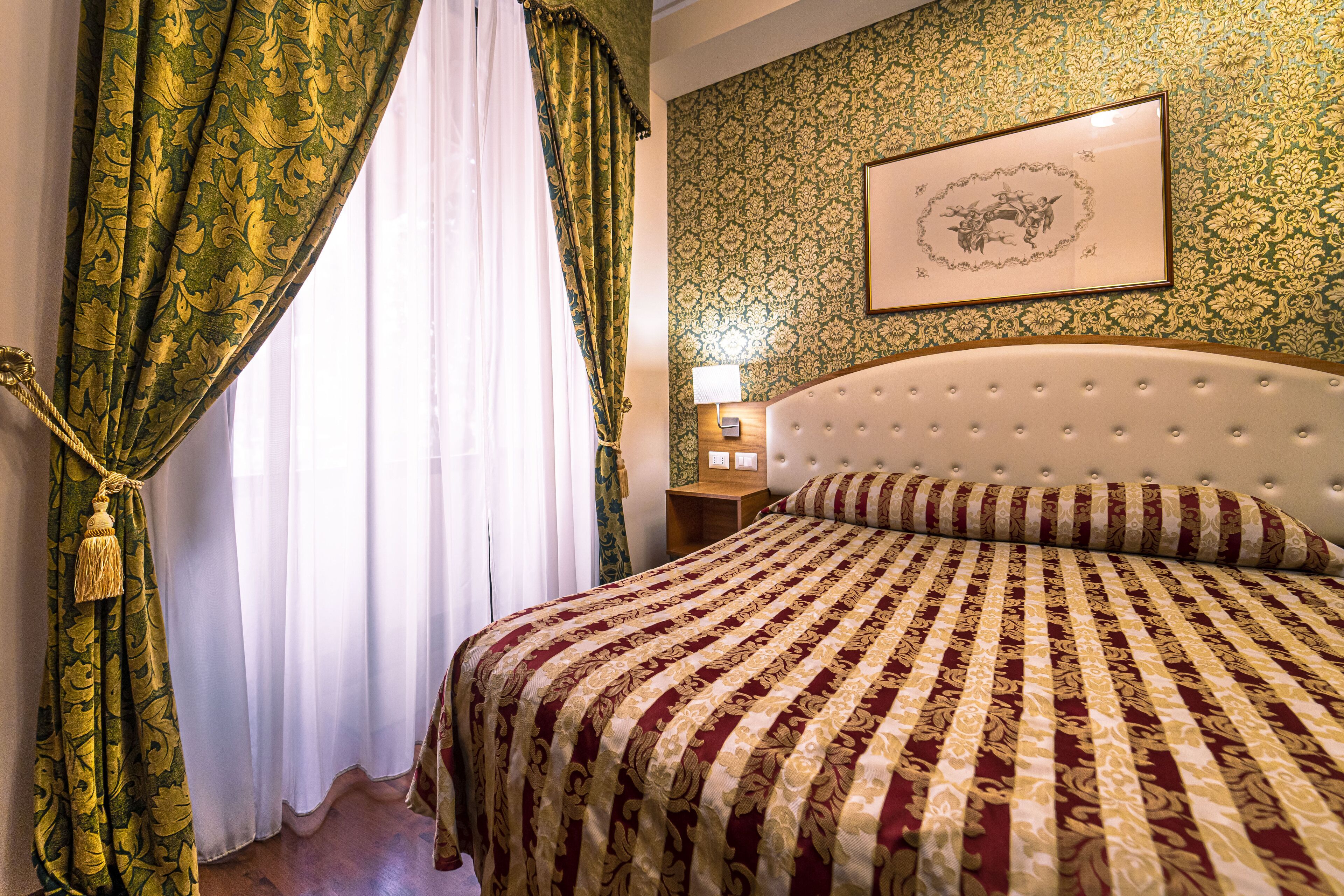 Una habitación de hotel con una cama grande, cabecero, mesita de noche con lámpara y un cuadro enmarcado en la pared.