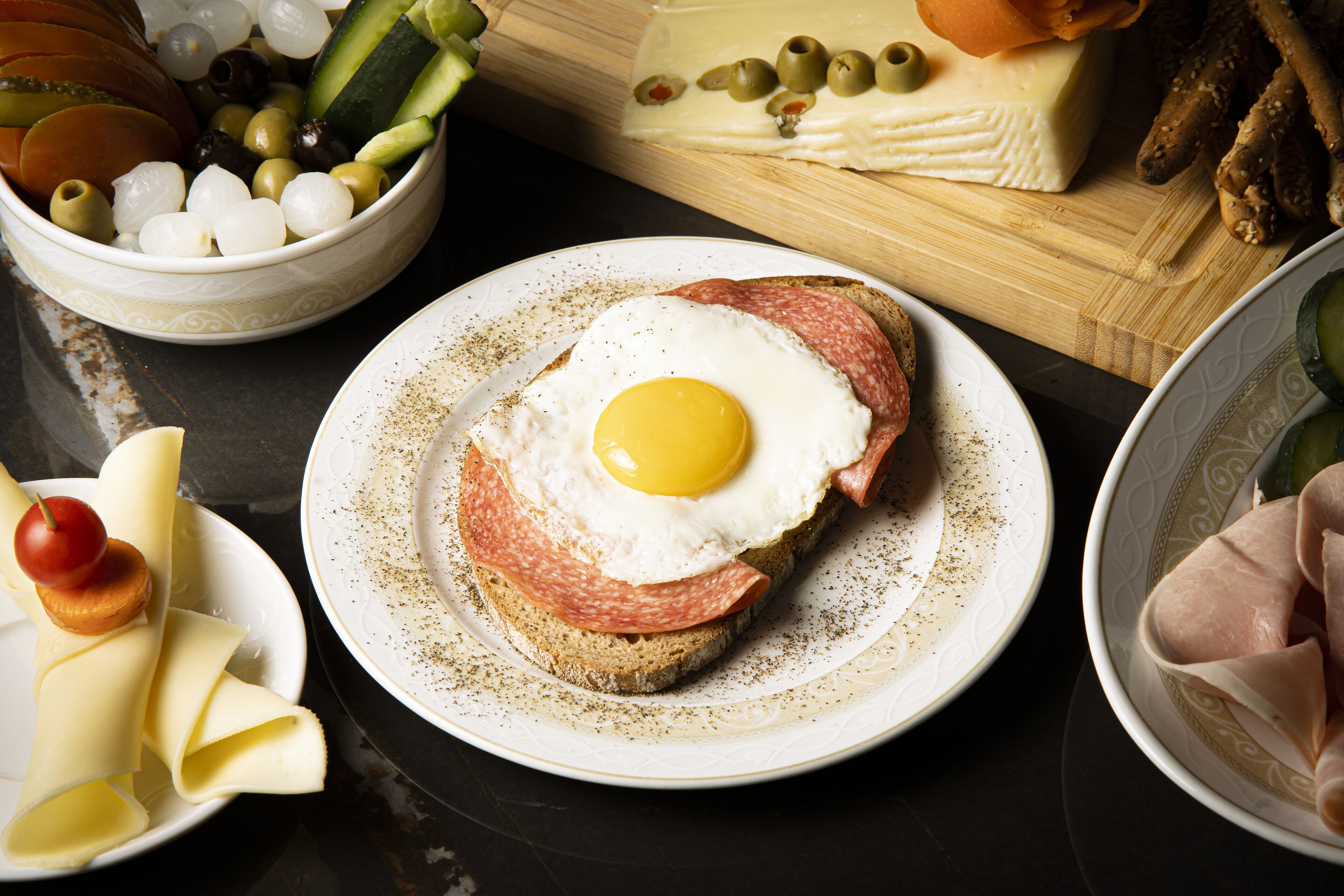 A breakfast plate with a fried egg, ham, and cheese on toast, surrounded by various condiments and ingredients.