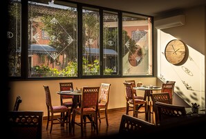 Un comedor con sillas y mesas de madera, ventanas amplias con vidrio decorativo y un reloj en la pared.