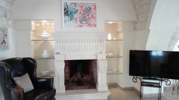 Una sala de estar con chimenea, un sofá de cuero negro, un televisor y estantes decorativos.