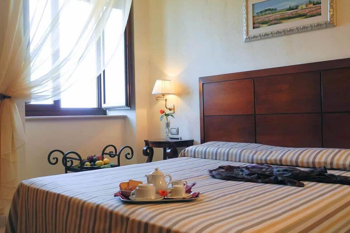 A hotel room with two beds, a dining table with breakfast items, a lamp, and a painting on the wall.
