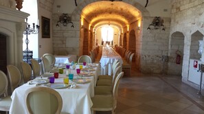 Una larga mesa de comedor dispuesta para una comida en una habitación con paredes de piedra y techo abovedado.
