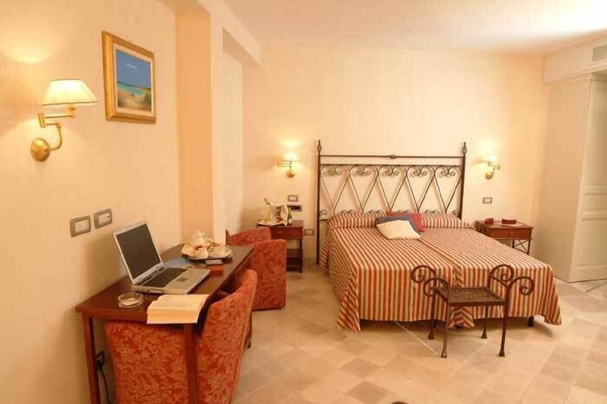A hotel room with a bed, a desk with a laptop, a chair, and a small table.