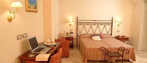 A hotel room with a bed, a desk with a laptop, a chair, and a small table.