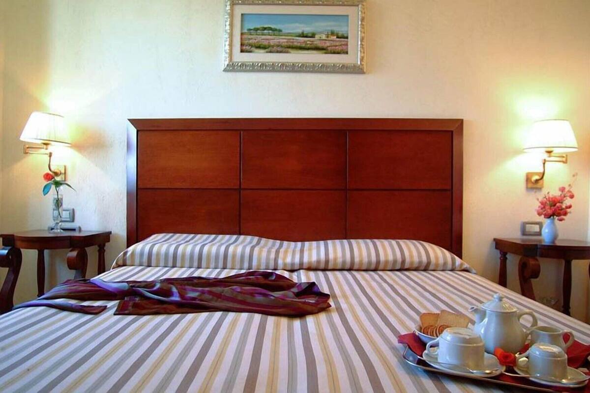 A hotel room with a bed, two bedside tables with lamps, a framed picture on the wall, and a tray with breakfast items.