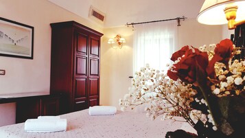 Ett hotellrum med en säng, en garderob, en vägglampa, ett fönster med gardiner och en inramad tavla på väggen.