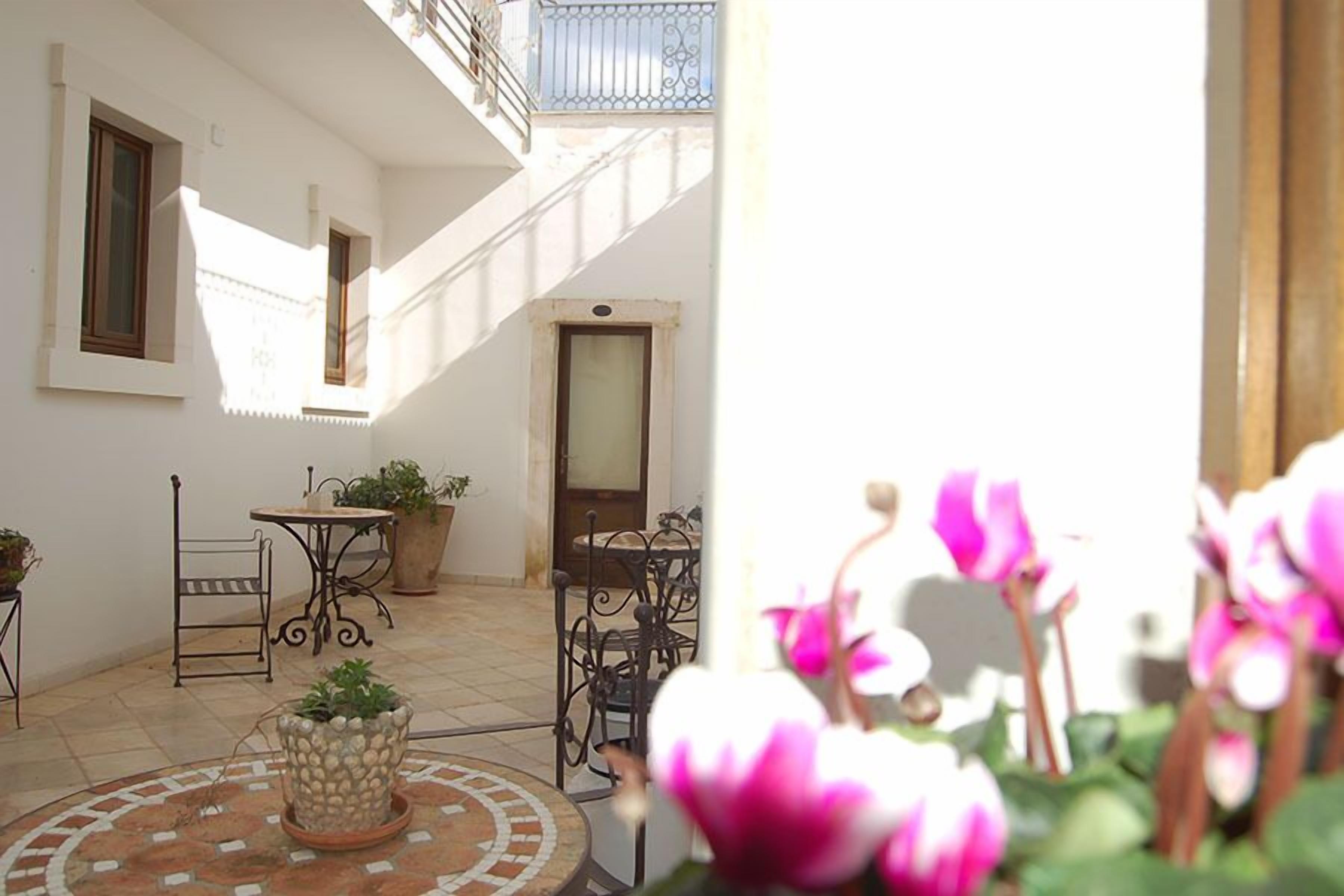 Une cour avec un sol carrelé, un escalier, une table avec des chaises et des plantes en pot.