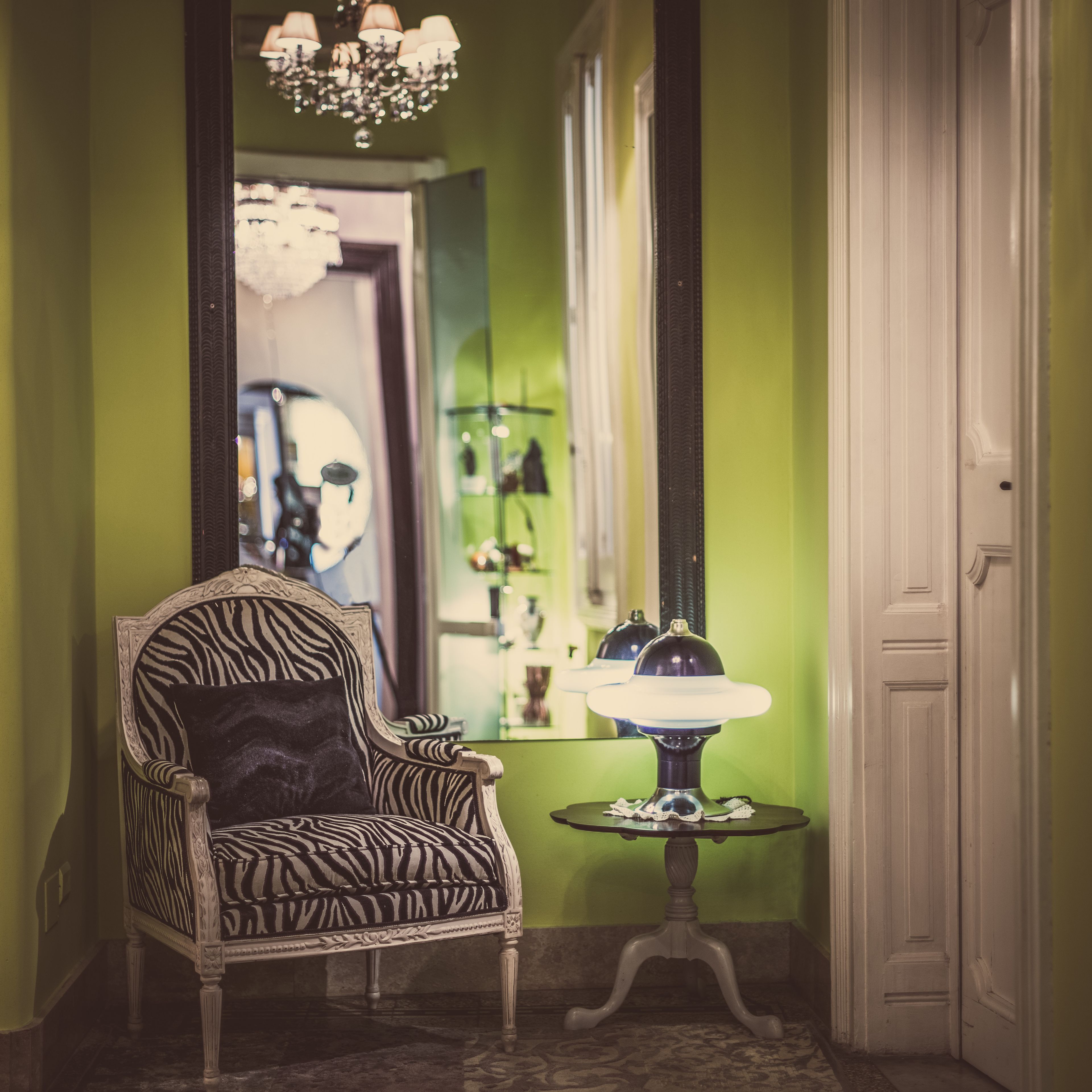 Une pièce comprenant un fauteuil à motifs zébrés, une table ronde avec une lampe et un miroir qui reflète un lustre.
