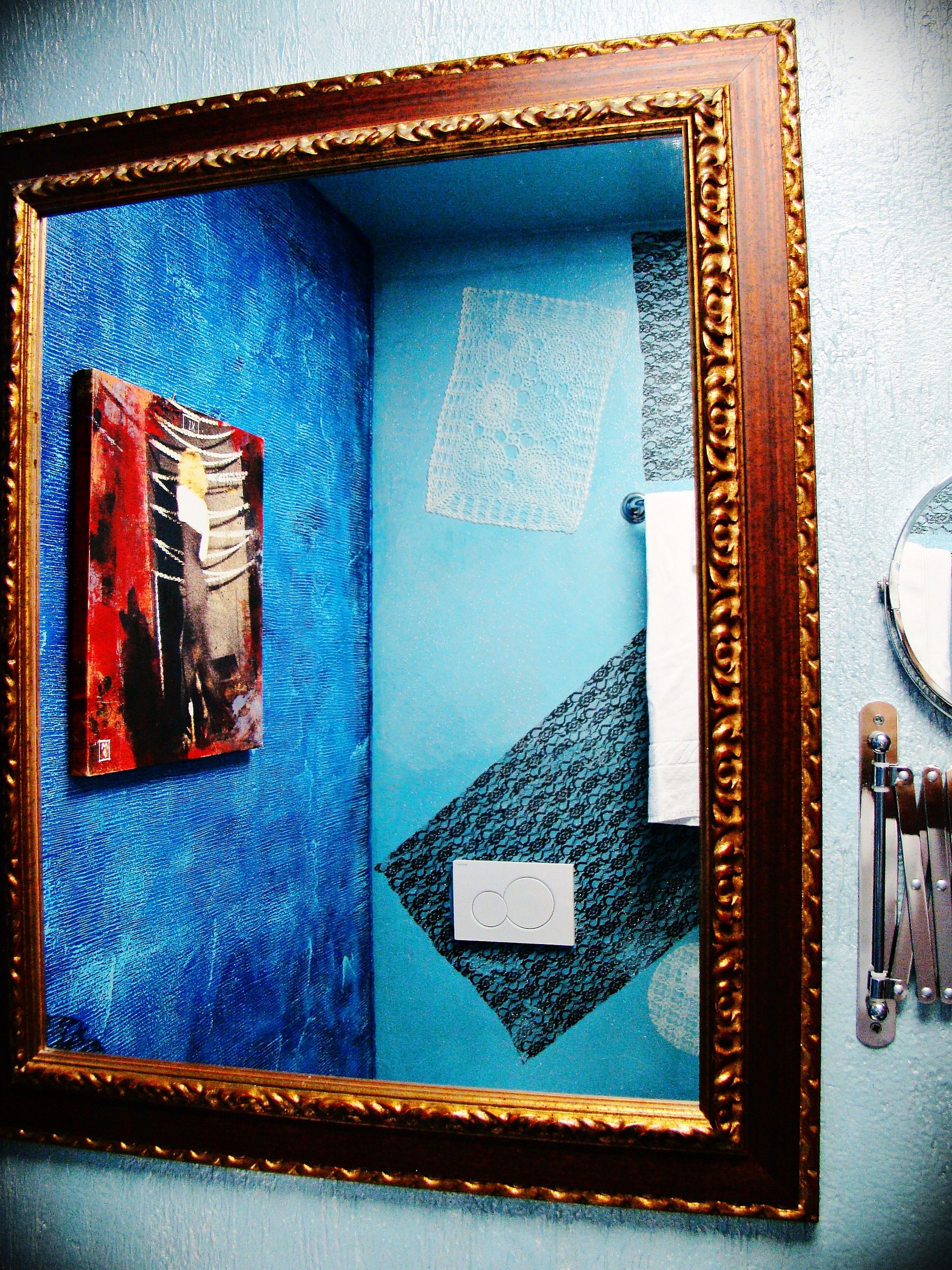 Een badkamer met een spiegel, een handdoekhouder en een kunstwerk in een lijst aan de muur.