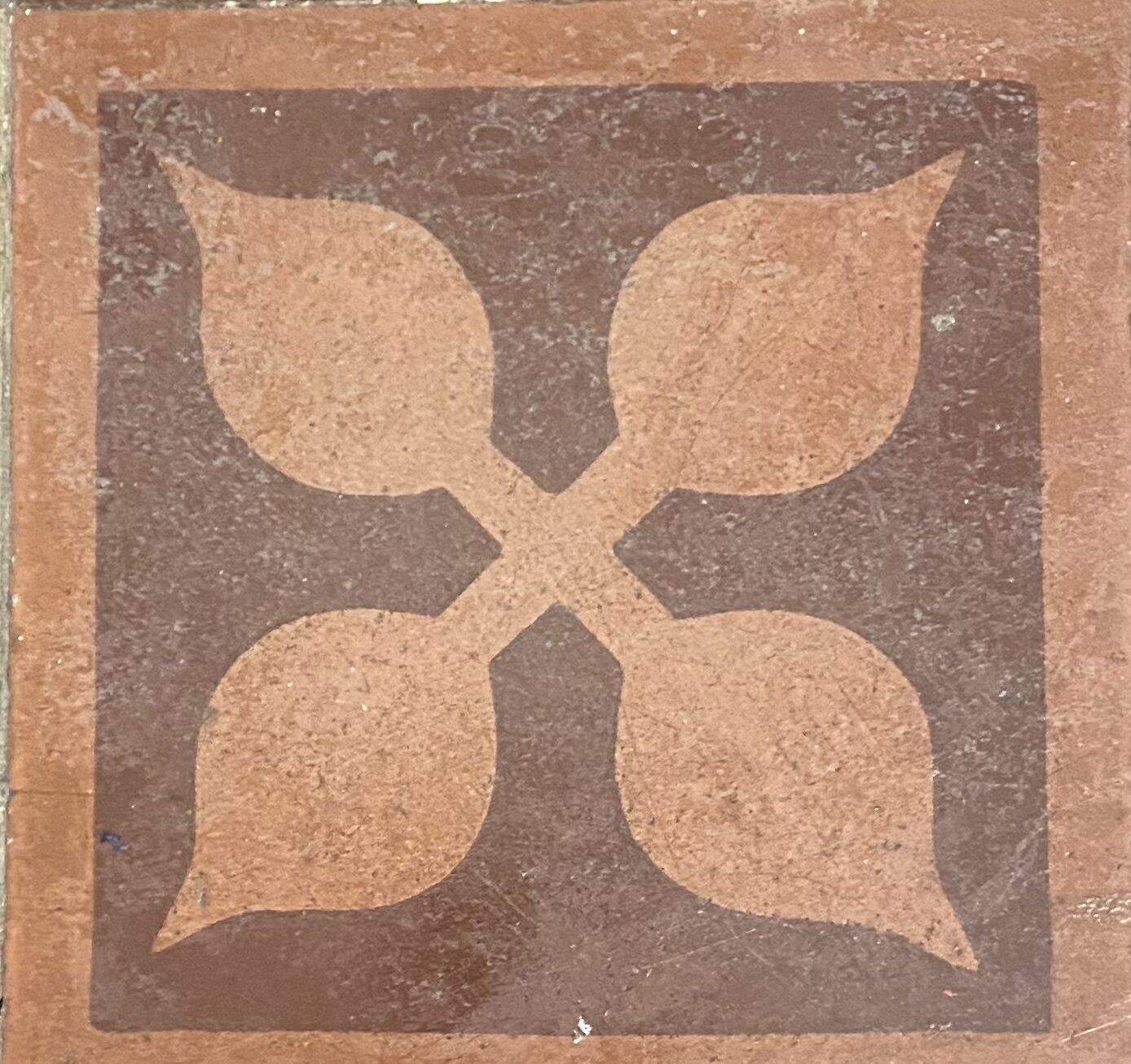A square tile with a symmetrical design featuring four leaf-like shapes.