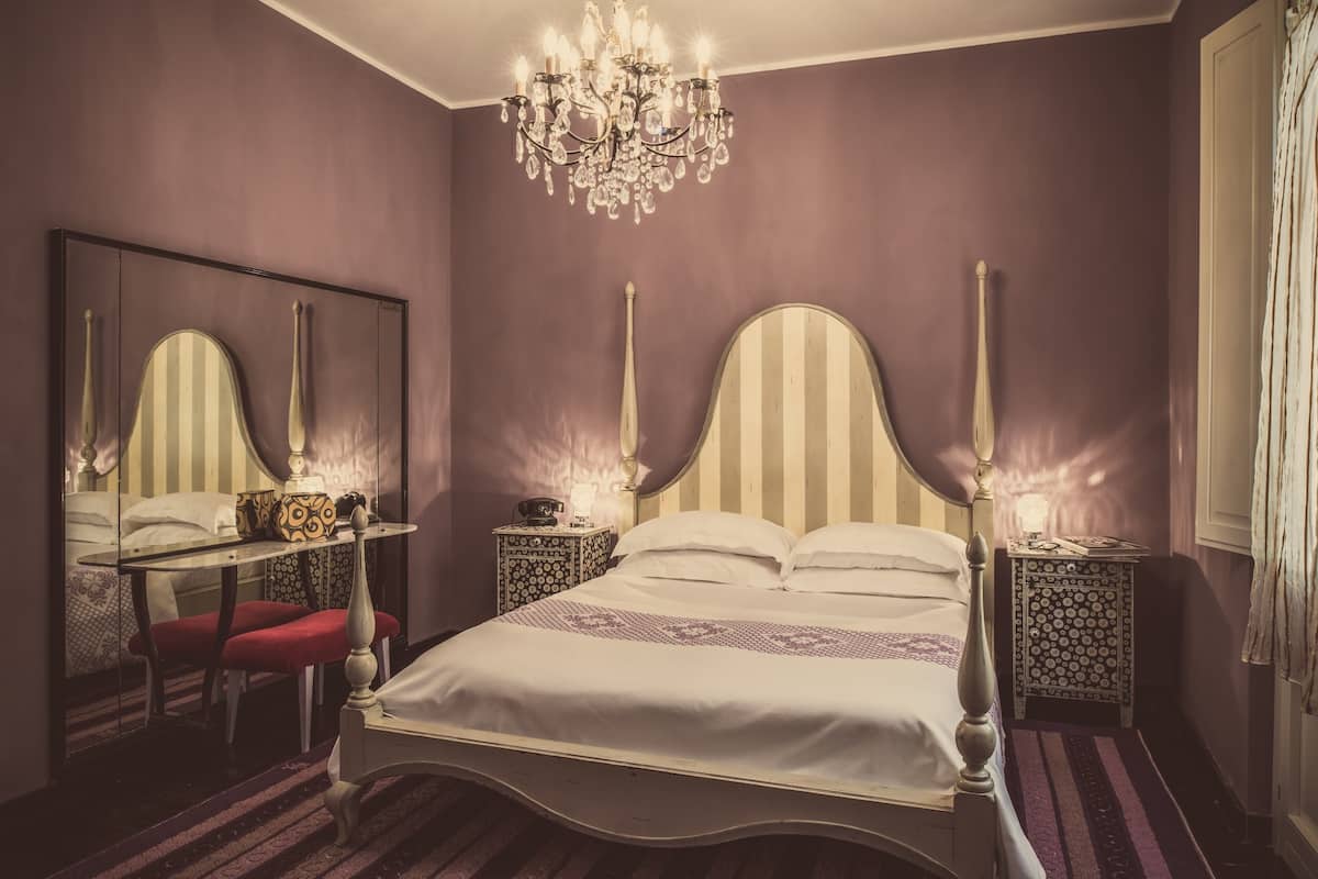 A bedroom with a large bed, a chandelier, a mirror, and patterned nightstands.