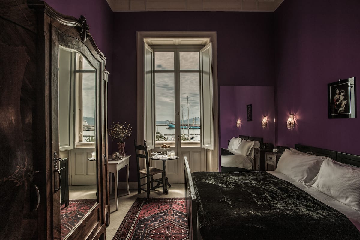 A bedroom with a large bed, a window with a view, a chair, a small table, and a dresser.