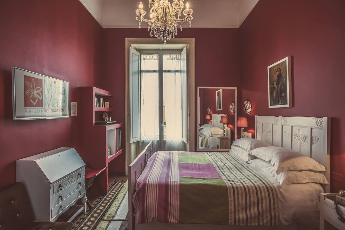 A bedroom with a bed, a dresser, a vanity, a chandelier, and a window.