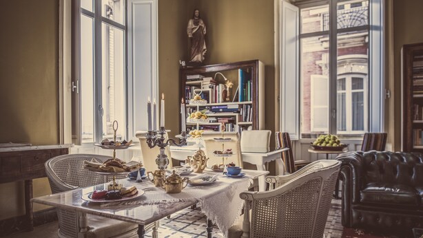 A dining area with a table set for a meal, surrounded by wicker chairs and a leather sofa.