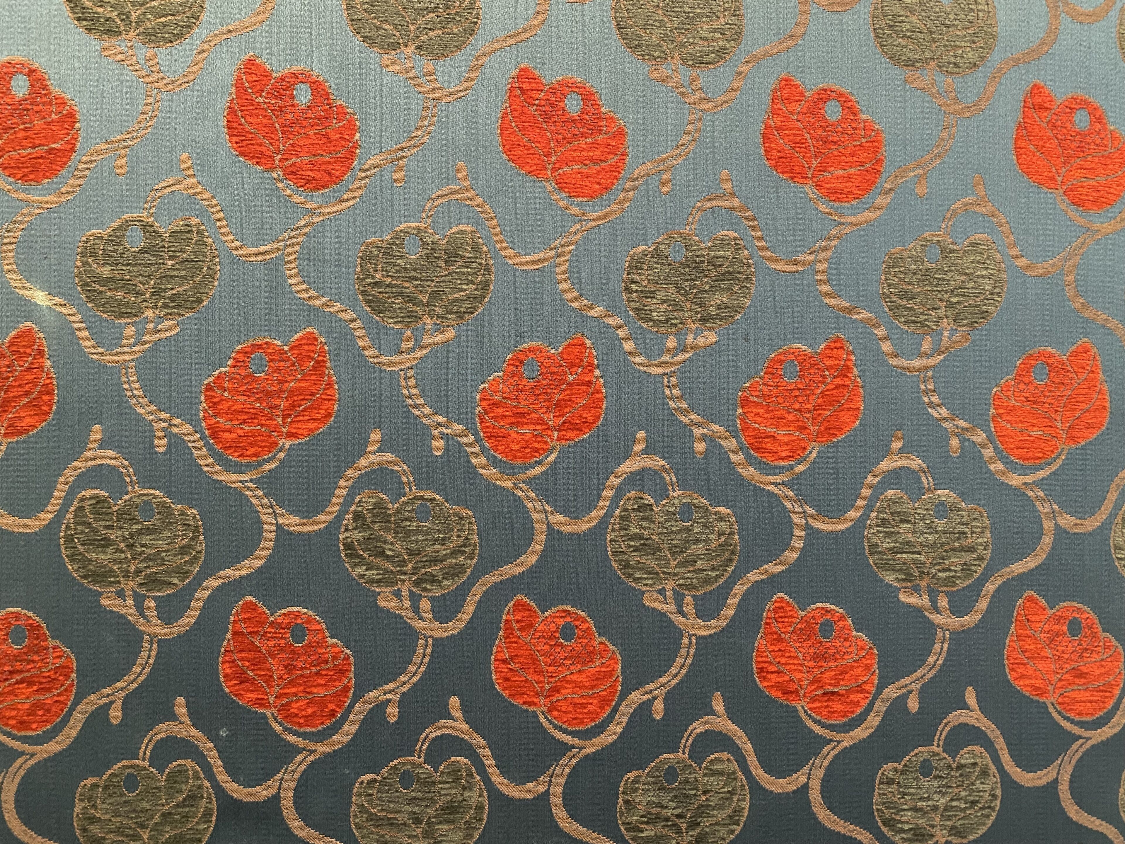 A fabric with a repeating pattern of red and green leaves on a blue background.