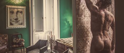 A room with a green wall, a chandelier, a framed artwork, a fireplace, and a mirror reflecting a person.