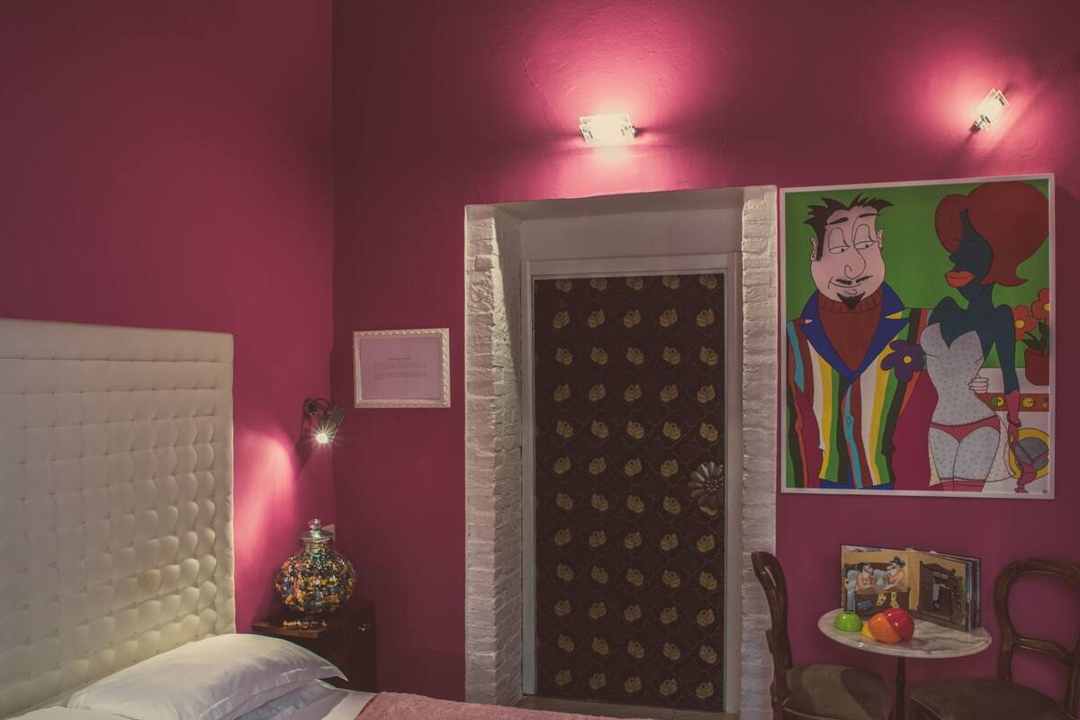 A bedroom with a bed, a nightstand, a chair, a small table, and a door.