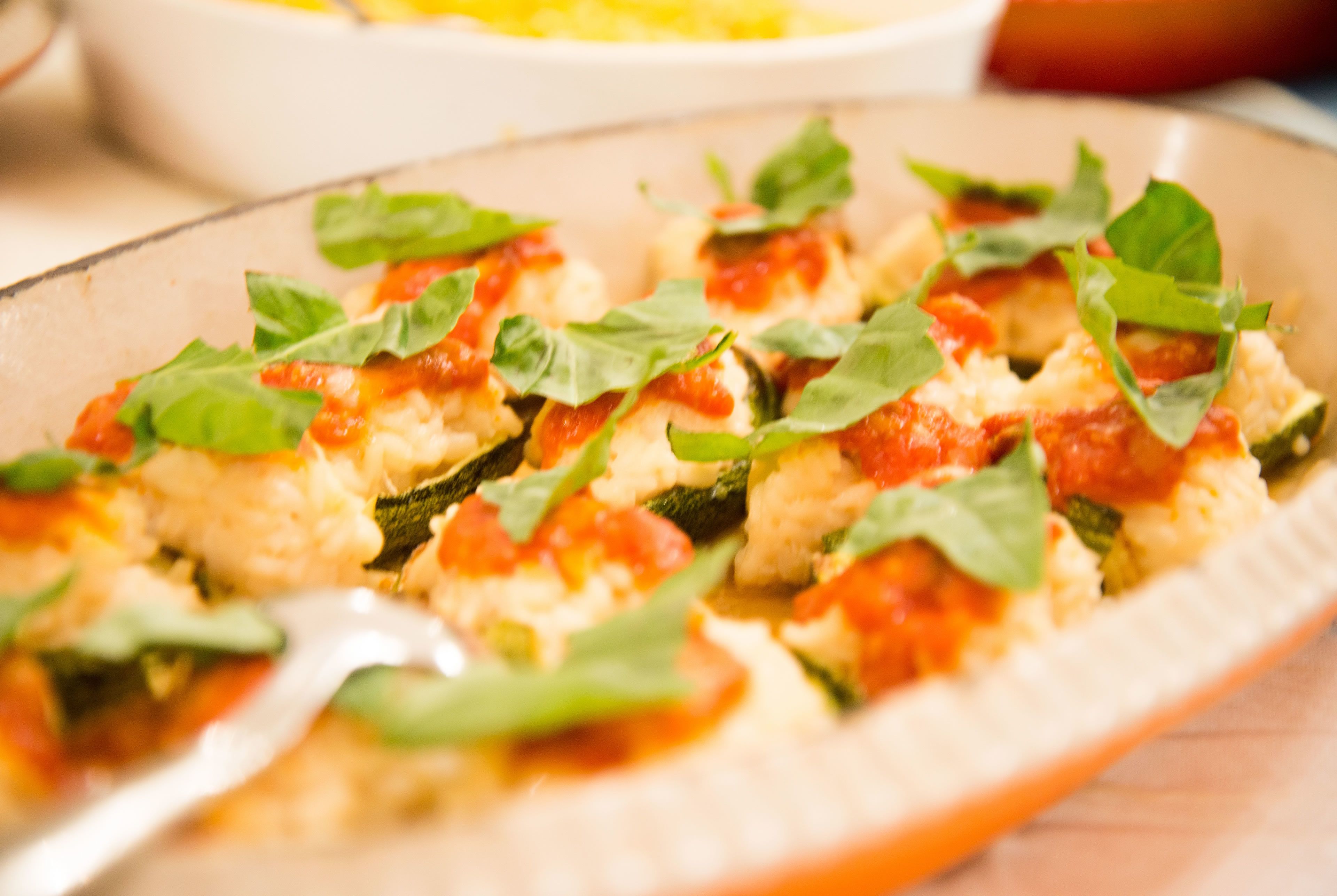 A plate of food with zucchini slices topped with cheese and tomato sauce, garnished with basil leaves.