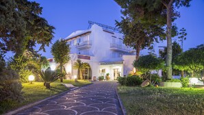 Un hôtel avec un chemin pavé menant à l’entrée, entouré de verdure et d’arbres.