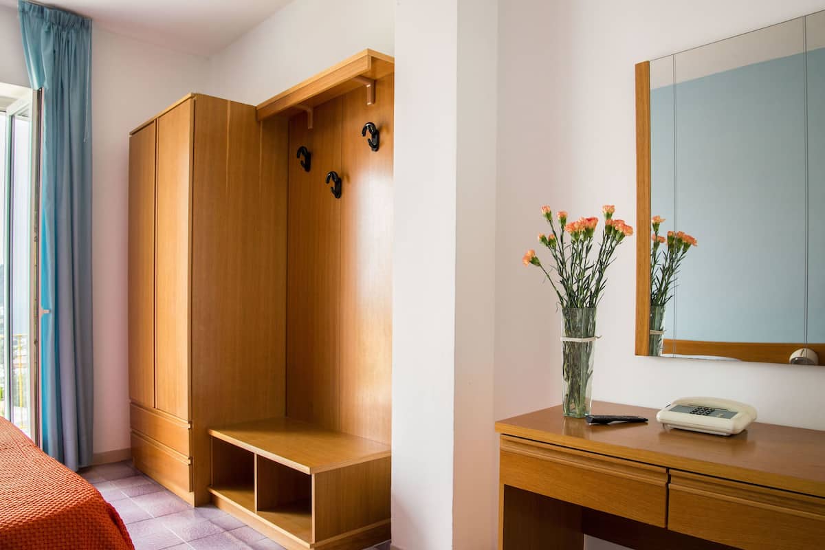 A hotel room with a wooden wardrobe, a bedside table with a vase of flowers, and a mirror on the wall.