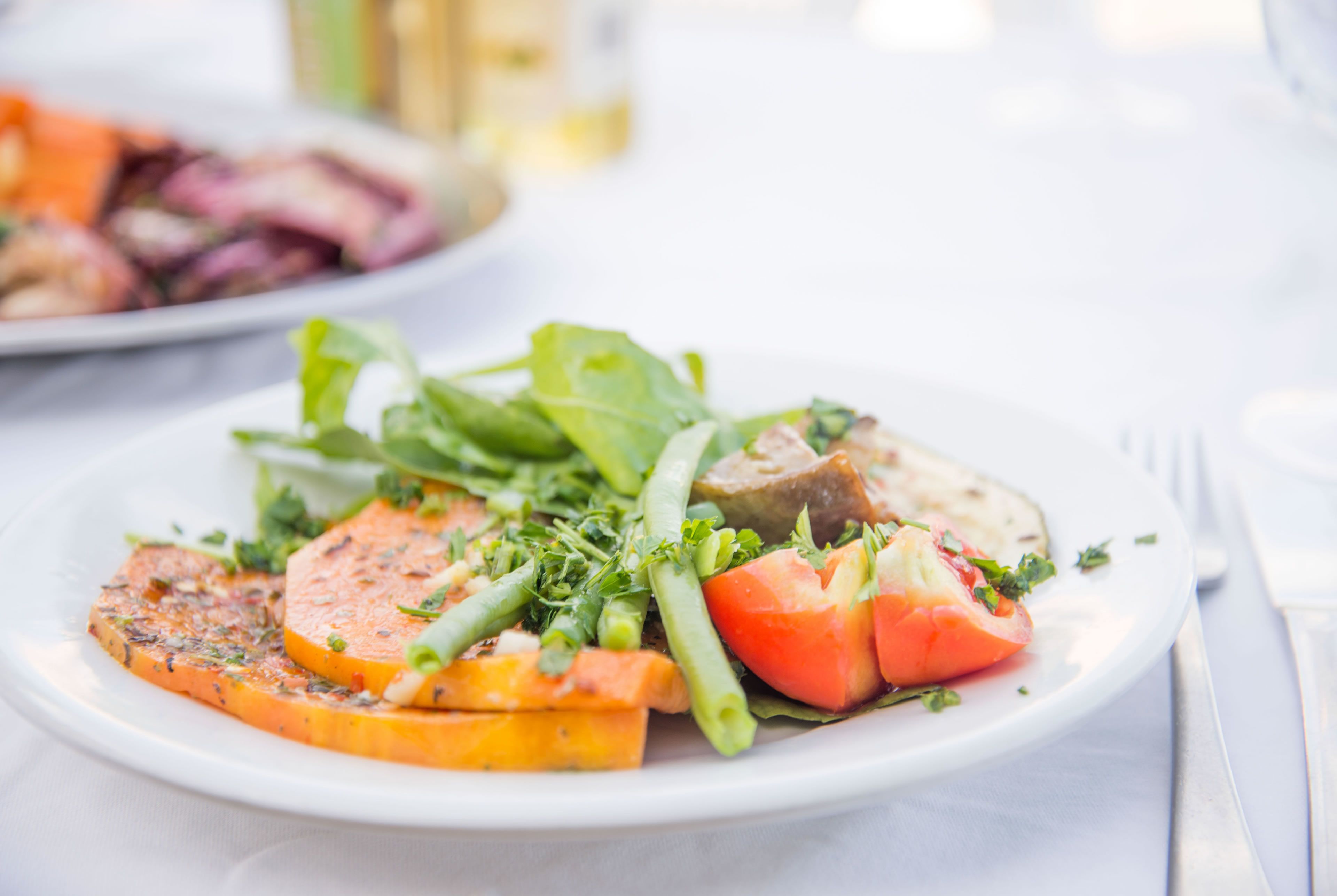 Un piatto di cibo con diversi tipi di verdura e un pezzo di carne, probabilmente salmone, su un piatto bianco.